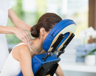 A woman sits in a massage chair and receives an upper body massage at the office.