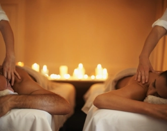 Two people receiving a candlelit couples massage from professional massage therapists.