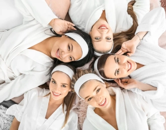Five women wearing white robes laying down and looking up at the camera together.